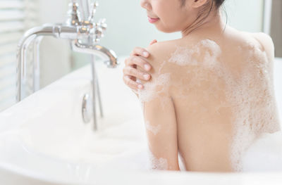 Rear view of topless young woman taking bath in bathtub