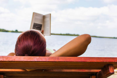 Woman relaxing on lounge chair at beach against sky