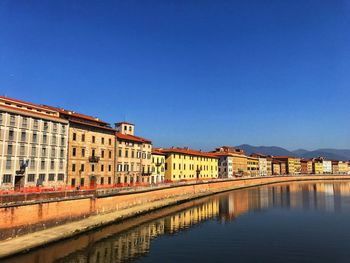 Reflection of buildings in river against clear blue sky