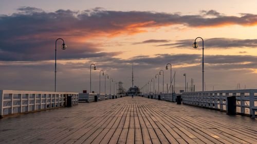 Empty footpath by pier against sky during sunset