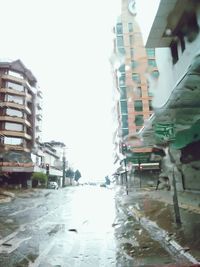 Wet street amidst buildings against sky in city