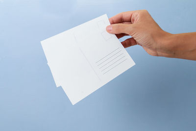 Close-up of hand holding paper against white background