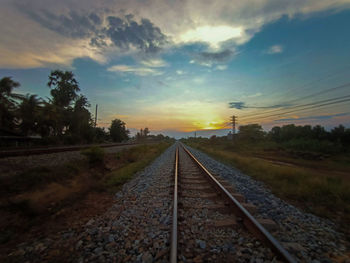 Surface level of railroad tracks against sky during sunset