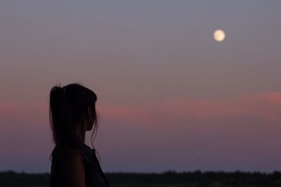 Woman looking at moon in sky during sunset