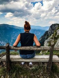 Rear view of woman sitting on bench against sky