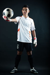 Full length of young man standing on soccer ball against black background