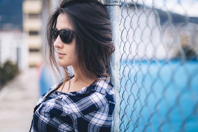 Portrait of beautiful young woman standing by fence