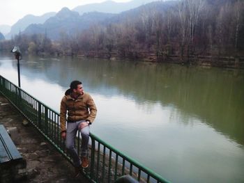 Man standing on railing by lake