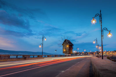 Light trails on road and illuminated wooden windmill at night in the city