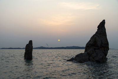 Rock formation in sea against sky during sunset