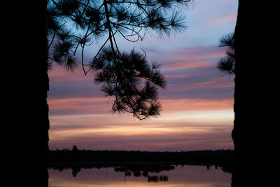 Silhouette trees by lake against romantic sky at sunset