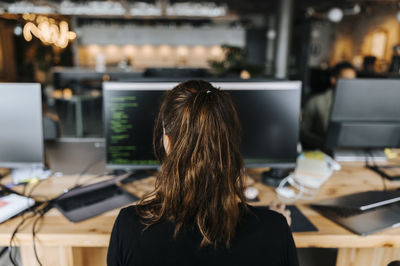 Rear of female coder with ponytail sitting at desk in office