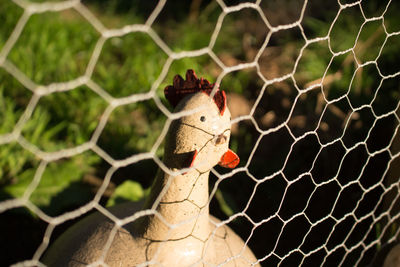 Close-up of chicken figurine by chainlink fence on field