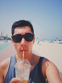Portrait of young woman drinking sunglasses at beach against clear sky