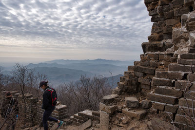 Rear view of man standing on mountain against cloudy sky