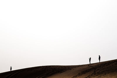 Silhouette people standing on sand dune