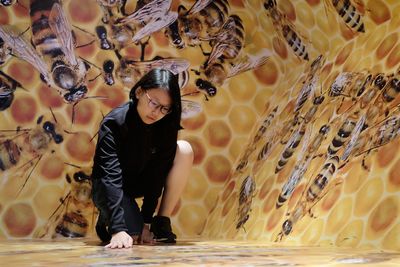 Full length of girl kneeling on floor against honey bee wallpaper