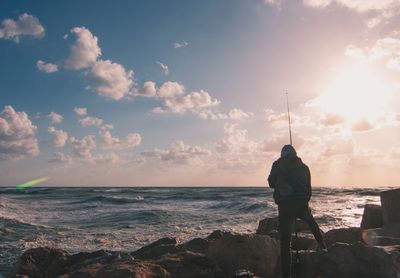 Man standing on rock by sea against sky