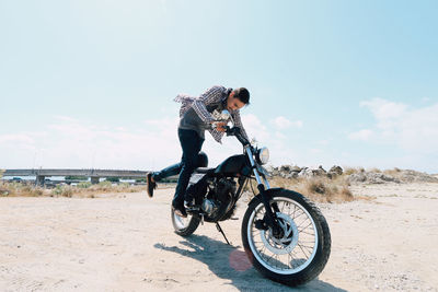 Young man riding bicycle on motorcycle against sky