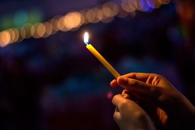 Cropped hand holding illuminated candle at night