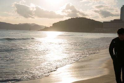 Rear view of man standing on beach against sky