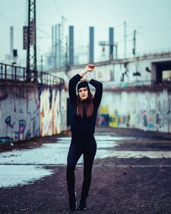 Full length portrait of young woman in city against sky