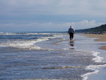 Rear view of man standing on beach against sky