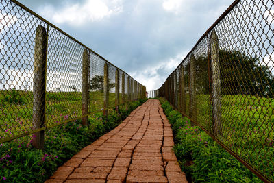 Footpath amidst fence against sky