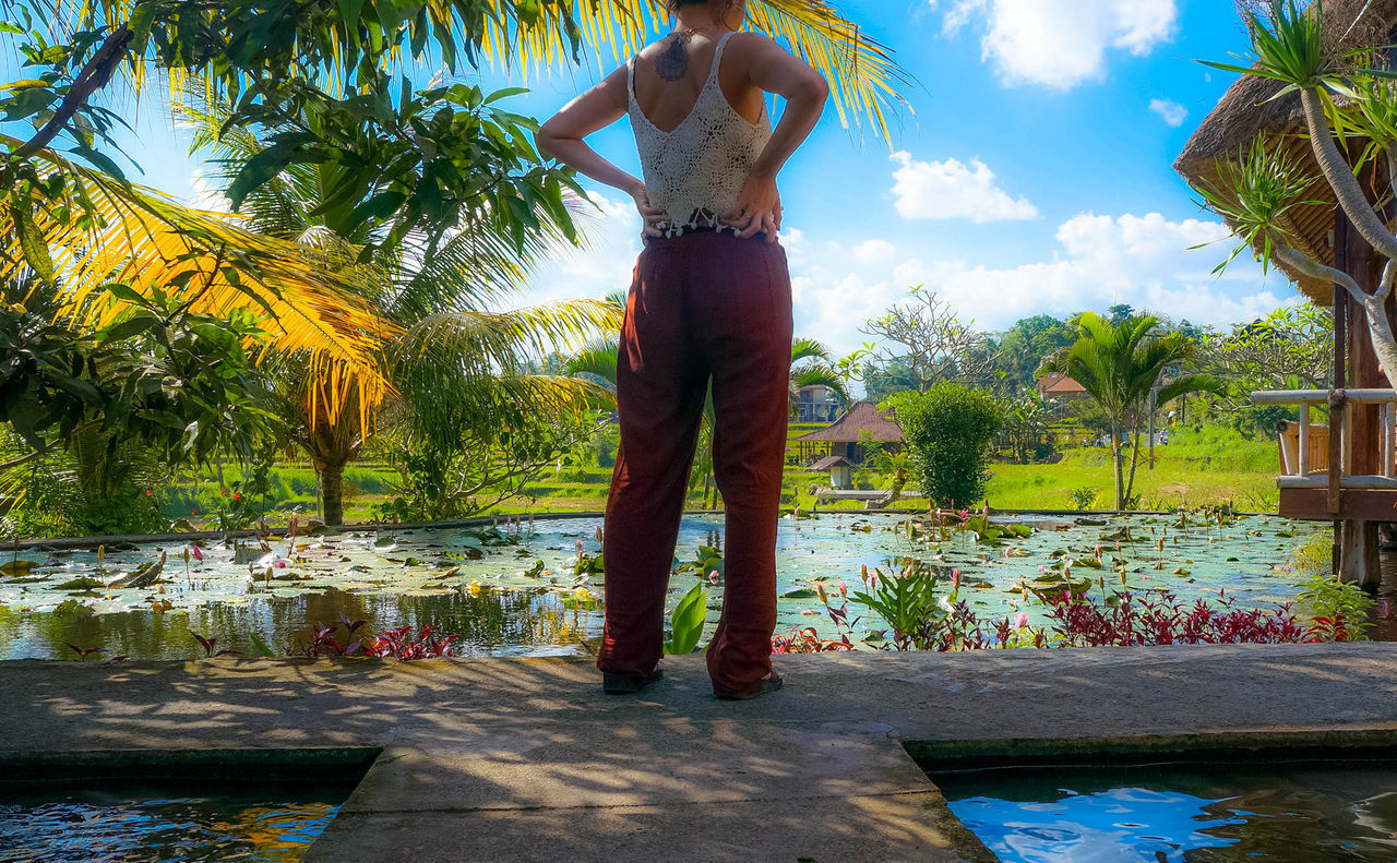 REAR VIEW OF MAN STANDING BY SWIMMING POOL AGAINST LAKE