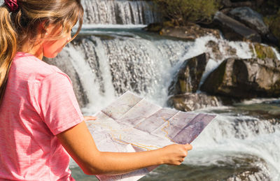 Midsection of woman holding paper at waterfall