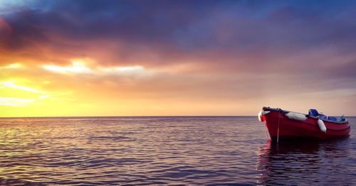 Boat in sea against cloudy sky during sunset