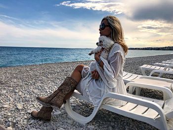 Woman sitting on beach by sea against sky