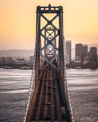 Bridge over river amidst buildings against sky during sunset