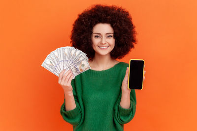 Portrait of smiling woman smart phone and cash against colored background