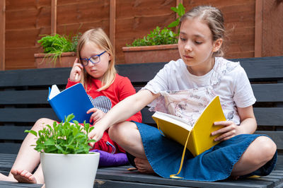 Two school age girls sitting together in garden and doing homework.