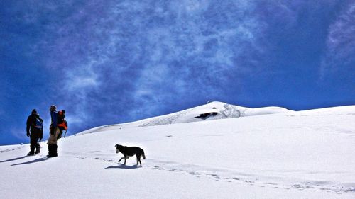 Full length of friends with dog on snow covered mountain against sky