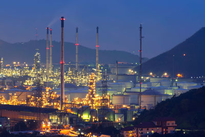 Illuminated factory in city against sky at night