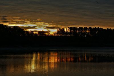 Silhouette trees by lake against sky during sunset