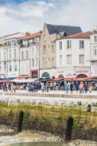 People on river by buildings in city against sky