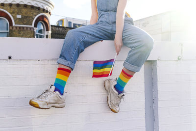 Transgender person with rainbow flag sitting on wall