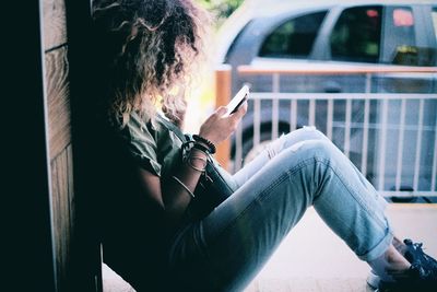 Side view of woman using cellphone while sitting on window