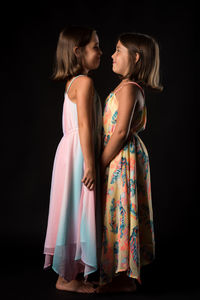 Side view of girl standing with sister on black background