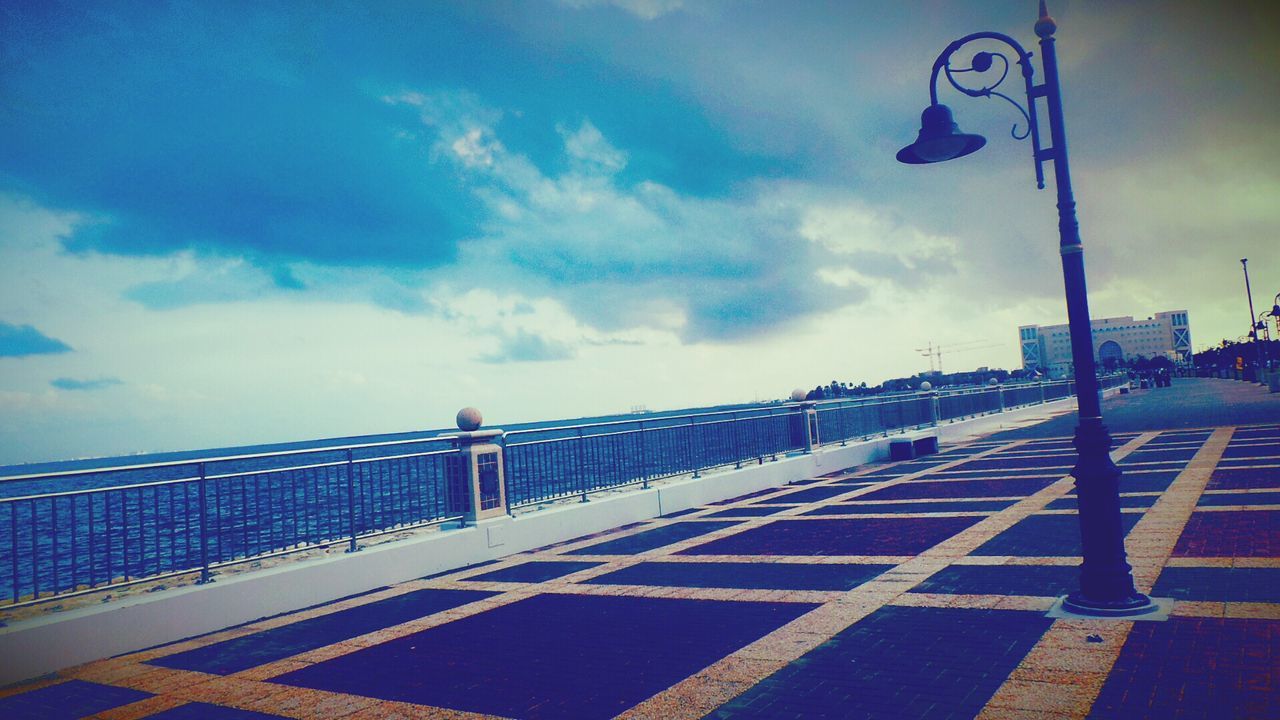 sky, built structure, architecture, cloud - sky, railing, street light, building exterior, blue, cloud, transportation, the way forward, city, outdoors, road, street, cloudy, empty, lighting equipment, incidental people, day