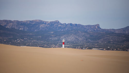 Lighthouse by sea and mountains against sky