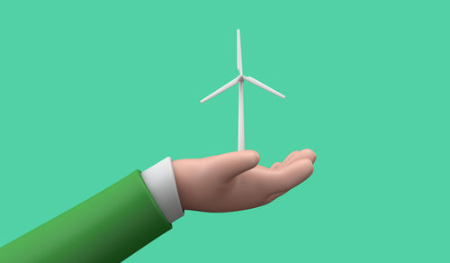 Hand holding wind turbine against blue background