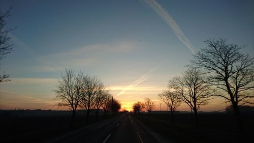 Road by silhouette trees against sky at sunset