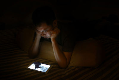 High angle view of young man using digital tablet on bed in darkroom