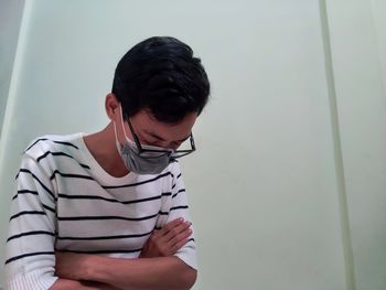 Young man looking away while standing against wall
