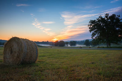 Hay bales on field against sky during sunset