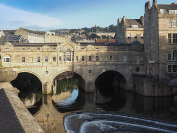 Arch bridge over river amidst buildings in city against sky